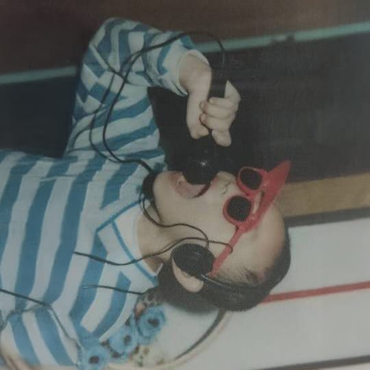 Childhood photograph of Yang Bohu wearing headphones and red sunglasses, singing into a microphone